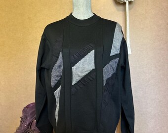 May include: Black sweater with grey geometric patterned design. The sweater has long sleeves and a crew neck.