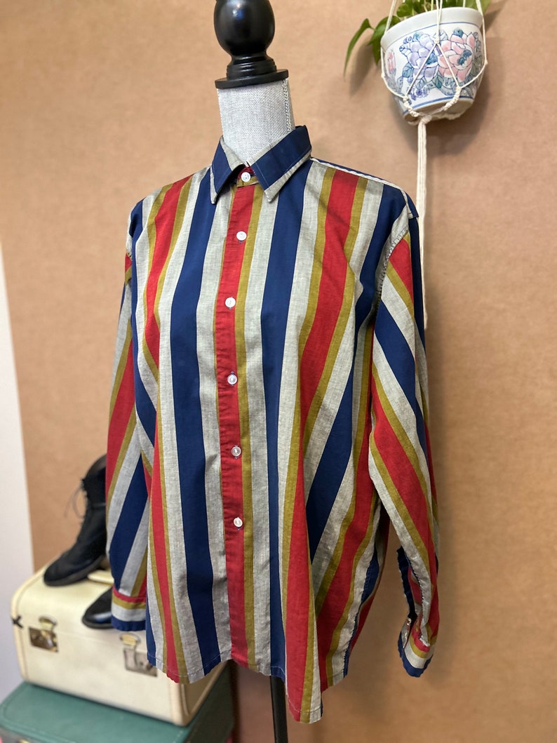 Peut inclure: Une chemise &agrave; manches longues &agrave; boutons avec des rayures diagonales en rouge, bleu, or et gris.