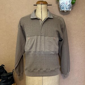 Op de afbeelding: Een bruin shirt met lange mouwen, een kraag en een knoopsluiting. Het shirt heeft een getextureerde, geribbelde stof op de mouwen en het lichaam, met een effen paneel over de borst. Het shirt wordt op een mannequin getoond.