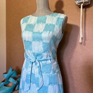 May include: A light blue dress with a white abstract pattern. The dress has a fitted bodice and a flowing skirt. The dress is tied at the waist with a matching sash.