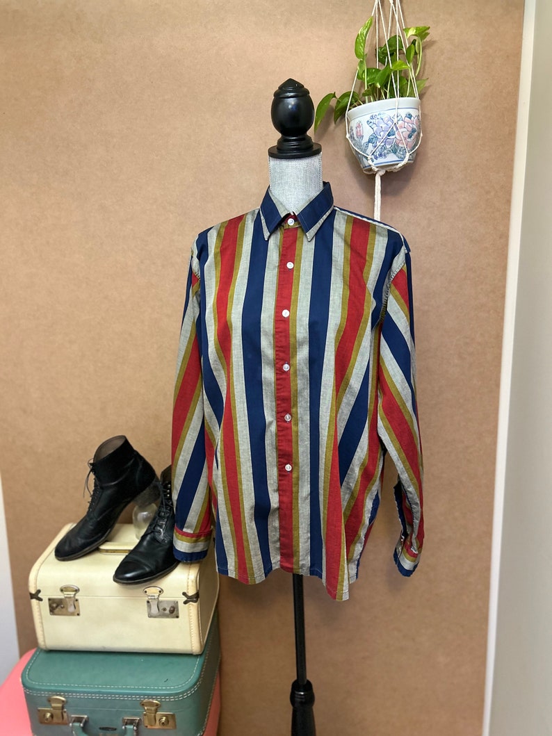 Peut inclure: Une chemise &agrave; manches longues &agrave; boutons avec des rayures verticales rouges, bleues, vertes et blanches. La chemise est sur un mannequin sur un fond brun.