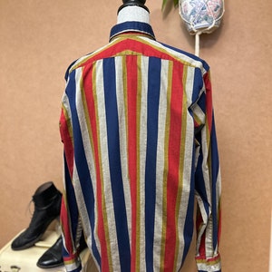 Peut inclure: Une chemise &agrave; manches longues &agrave; boutons avec des rayures verticales rouges, bleues, dor&eacute;es et beiges.