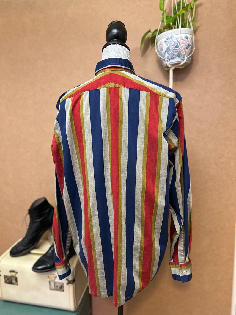 Peut inclure: Une chemise &agrave; manches longues &agrave; boutons avec des rayures verticales rouges, bleues, dor&eacute;es et beiges.