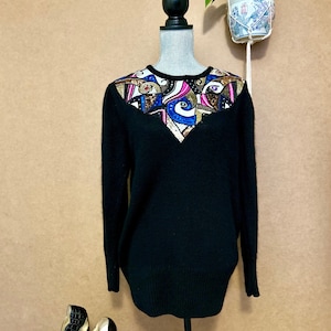 May include: Black sweater with a colourful, sequined design on the neckline. The design features blue, pink, gold, and white elements. The sweater is displayed on a mannequin.