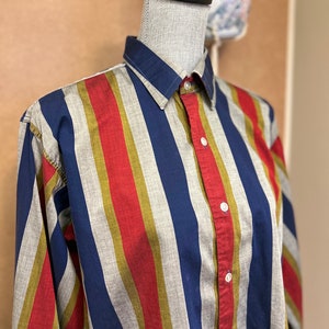 Peut inclure: Une chemise &agrave; boutons ray&eacute;e avec des rayures bleues, rouges, dor&eacute;es et grises. La chemise est sur un mannequin.