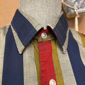 Peut inclure: Une chemise &agrave; boutons ray&eacute;e avec des rayures bleues, rouges, vertes et grises. La chemise a un col et deux boutons.