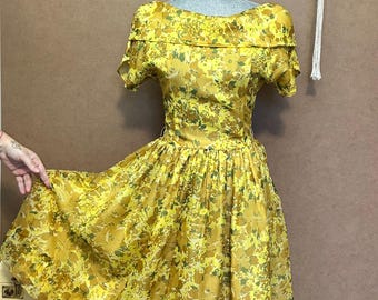 May include: A yellow floral dress with a fitted bodice and a full skirt. The dress has a scoop neckline and short sleeves.