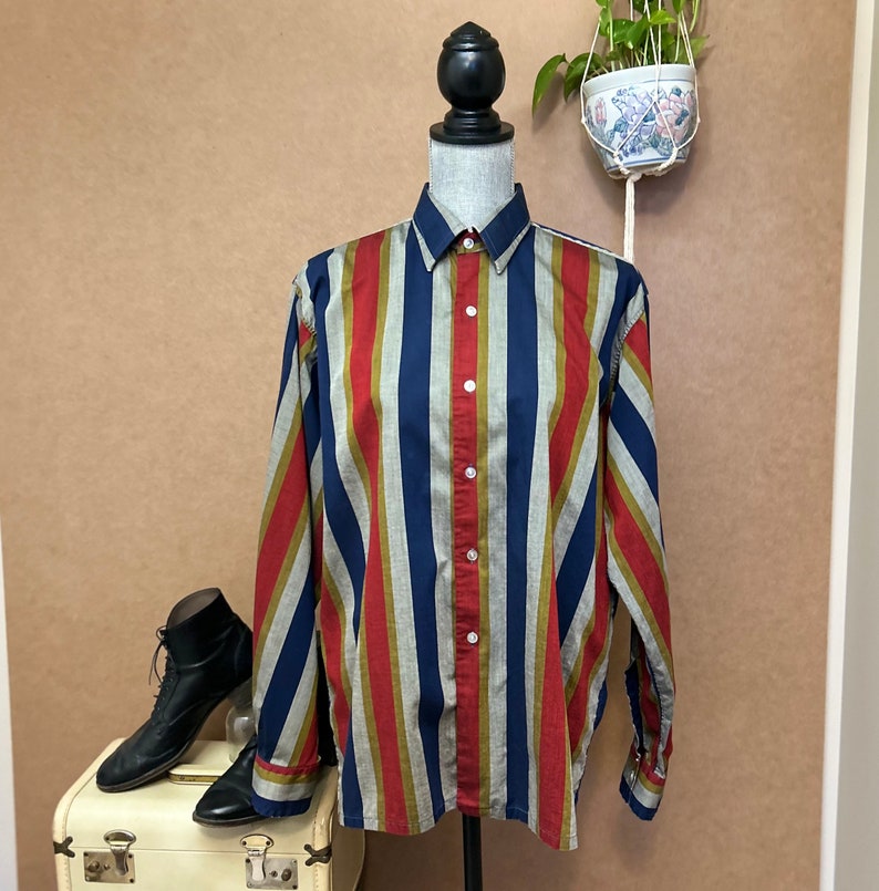 Peut inclure: Une chemise &agrave; manches longues &agrave; boutons avec des rayures verticales rouges, bleues et vertes. La chemise est faite d'un tissu l&eacute;ger et a une coupe d&eacute;contract&eacute;e.