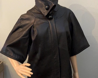May include: A black leather jacket with a high collar and short sleeves. The jacket has two large buttons on the front.