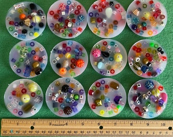 May include: Ten clear round resin coasters with colorful beads and other small objects embedded inside. The coasters are arranged in two rows of five.