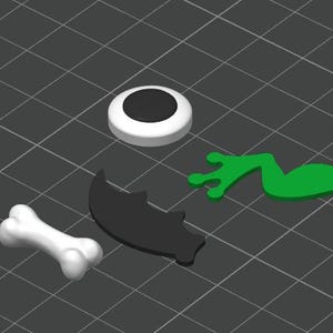 May include: A collection of four distinct flat components including a white bone shape, a black bat silhouette, a green frog leg shape, and a circular white disc with a black centre, all arranged on a dark grey grid background.