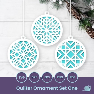 Pode incluir: Três ornamentos de papel redondos e brancos com um design de floco de neve. Os ornamentos estão pendurados em cordas brancas contra um fundo de madeira branca. O texto "Quilter Ornament Set One" está na parte inferior da imagem.