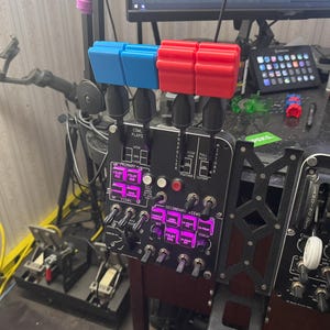 Könnte beinhalten: Ein schwarzes Flugsimulator-Bedienfeld mit mehreren Schaltern, Knöpfen und Hebeln. Das Panel hat blaue und rote Hebelkappen. Der Text auf dem Panel enthält "PRIMARY", "SECONDARY" und "FLAPS".