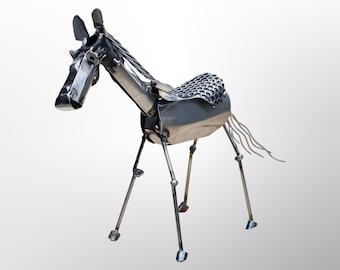 May include: A silver metal sculpture of a horse with a detailed, textured saddle. The horse has a long, flowing tail and is standing on four legs.