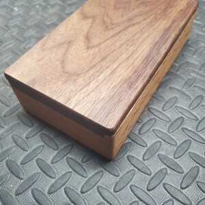 May include: A wooden box with a dark brown lid and a lighter brown base. The lid is made of walnut wood and has a smooth, polished finish.