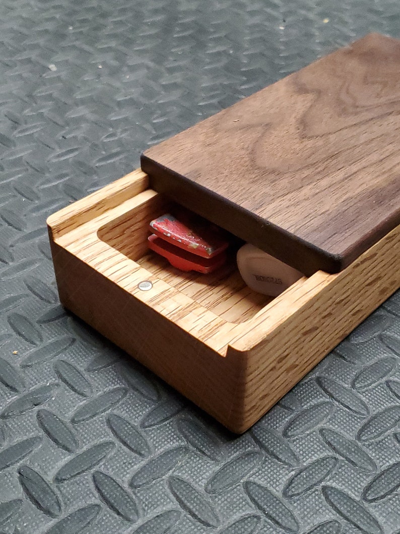 May include: A wooden box with a hinged lid, made of walnut and oak wood. The box is open, revealing a red and black object inside.