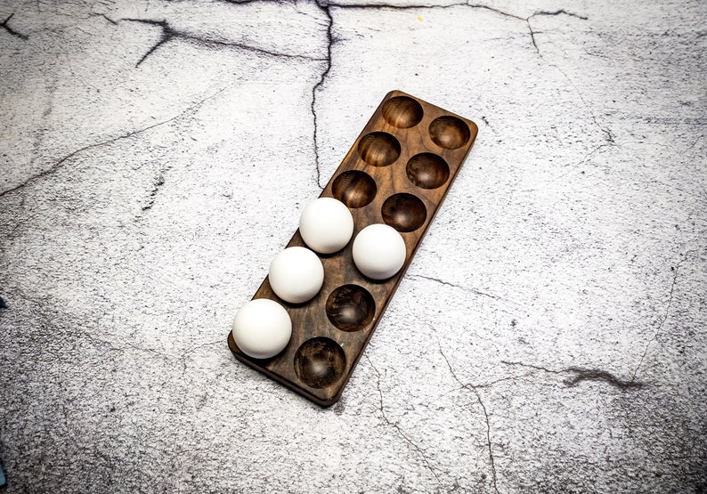 May include: A wooden egg holder with 18 compartments, filled with 5 white eggs.