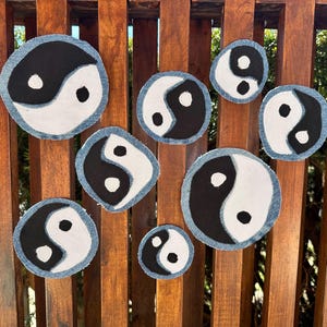 May include: A collection of yin yang patches in various sizes. Each patch features a black and white yin yang symbol with a denim blue border. The patches are arranged on a wooden surface.