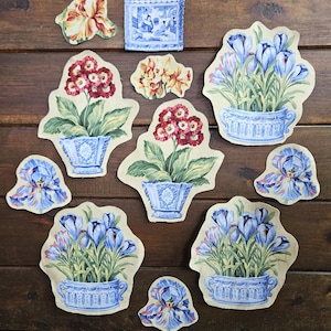 May include: A collection of fabric cutouts featuring botanical illustrations of blue and red flowers in blue and white decorative pots, along with individual iris and crocus flower motifs on a beige background, arranged in a scattered layout.