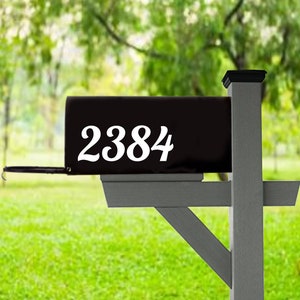 May include: Black mailbox with white numbers 2384 on the front. The mailbox is mounted on a gray wooden post.