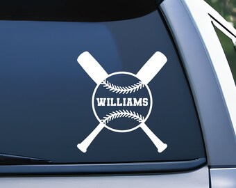 May include: A white vinyl decal applied to a vehicle rear window featuring a graphic of two crossed baseball bats behind a baseball. The center of the baseball contains the text WILLIAMS in bold, white, capital, sans-serif lettering.