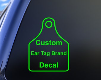 May include: A bright neon green decal shaped like a livestock ear tag, featuring a circular hole at the top. The text Custom Ear Tag Brand Decal is printed in a bold, sans-serif font in the center of the tag, applied to a dark glass surface.