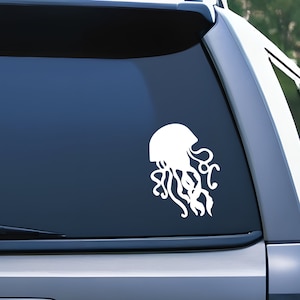May include: White vinyl decal of a jellyfish silhouette. The jellyfish is facing to the right and has a bell-shaped head and long tentacles.
