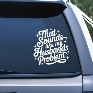 May include: White vinyl decal with the text "That Sounds like my Husbands Problem" in a whimsical font. The decal is affixed to a car window, showcasing a humorous statement.