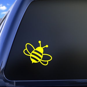 May include: A yellow bee decal on a black car window. The bee has black stripes and is facing to the right.