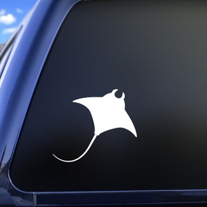 May include: A white silhouette of a manta ray, a type of ray fish, is displayed on a dark blue car window. The silhouette is facing right and has a long tail.
