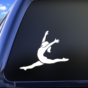 May include: White vinyl decal of a gymnast in a split leap, arms raised. The silhouette is applied to a dark surface, likely a car window. The gymnast's ponytail is visible. A dynamic image for sports enthusiasts.