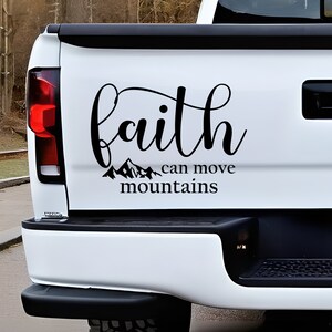 Könnte beinhalten: Schwarzer Vinyl-Aufkleber auf einer weißen LKW-Heckklappe. Der Aufkleber zeigt das Wort "faith" in einer geschwungenen Schriftart, darüber der Satz "can move mountains" in kleinerer Schrift. Eine Bergkette befindet sich zwischen den beiden Sätzen.
