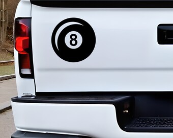 May include: Black vinyl decal of an eight ball, a classic symbol from the game of pool. The number 8 is prominently displayed in white within the black ball. The decal is affixed to the white tailgate of a truck.