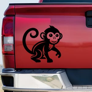 May include: Black monkey decal with a smiling face and a long, curled tail. The monkey is depicted in a cartoon style, with a simple, clean design. The decal is applied to a red vehicle.