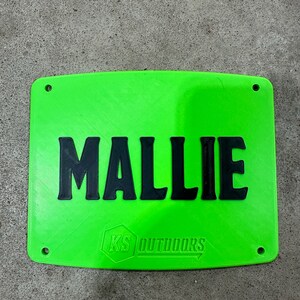 May include: A bright green sign with rounded corners and black holes in each corner. The sign says "MALLIE" in large black letters and has a small hexagonal logo that says "KS OUTDOORS" in the bottom center.