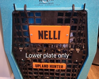 May include: A blue speckled dog crate with a black wire front. An orange plate with the name "NELLI" is attached to the front. Below, another orange plate reads "UPLAND HUNTER". The crate is made by Ruff Land Performance Kennels.