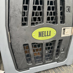 May include: A black and gray dog crate with a green oval label that says "NELLI OUTDOORS".