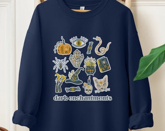 May include: A navy blue sweatshirt with a graphic print of various spooky and mystical symbols, including a cat, a snake, a pumpkin, a crystal, a witch's hat, and a skull. The text "dark enchantments" is printed below the graphic.
