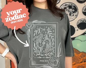 May include: A grey oversized t-shirt with a white graphic of a Pisces zodiac sign featuring two fish swimming in a circle with leaves and flowers. The text "your zodiac sign here" is on a red circle above the graphic.
