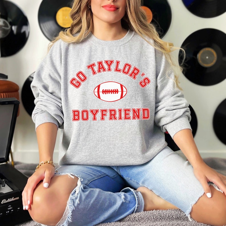 May include: Gray sweatshirt with red text that says "Go Taylor's Boyfriend" with a red football graphic.