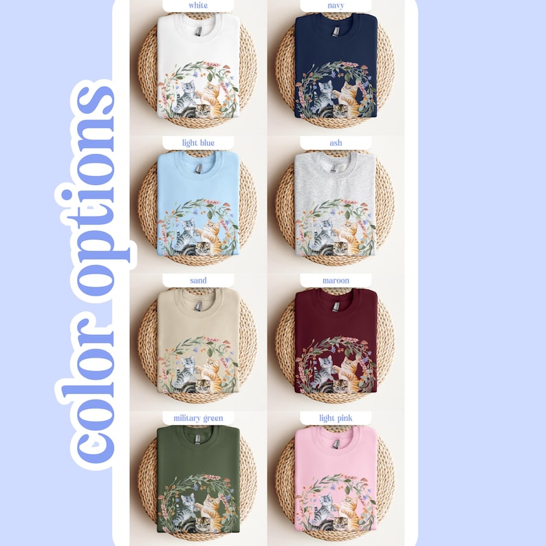 May include: A range of colour options for a sweatshirt featuring a graphic of three cats in a floral wreath. The colours include white, navy, light blue, ash, sand, maroon, military green, and light pink.