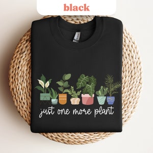 May include: Black t-shirt with a graphic of potted plants and the text "just one more plant".