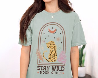 May include: A light green t-shirt with a graphic design of a leopard sitting in a crescent moon arch with stars. The text "Stay Wild Moon Child" is printed below the graphic.