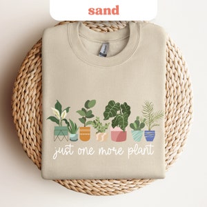 May include: A beige sweatshirt with a graphic of potted plants and the text "just one more plant".