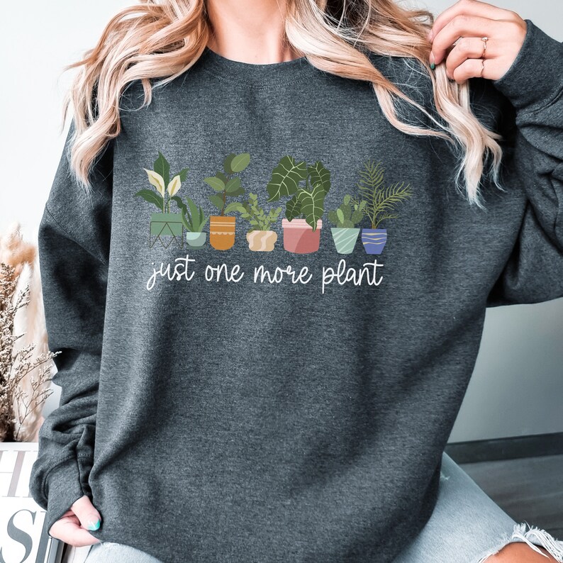 May include: A dark gray sweatshirt with a white graphic of potted plants and the text "just one more plant".