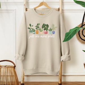 May include: A beige sweatshirt with a graphic of potted plants and the text "just one more plant".
