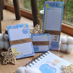 Può includere: Un set di blocchi note blu e bianchi con un'illustrazione fantasiosa di una bottiglia con stelle e una luna crescente. I blocchi note sono etichettati "Note", "Da fare" e "Pozione dei sogni".