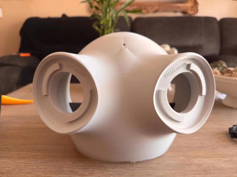 May include: A matte white, dome-shaped object with two circular openings on the sides. The left opening is embossed with the text LEFT HORN, and the right opening is embossed with the text RIGHT HORN. The object has a smooth, curved surface.
