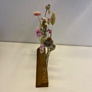 Op de afbeelding: Een houten bloemenhouder met een driehoekige basis en meerdere gaten voor gedroogde bloemen. De houder is gevuld met gedroogde bloemen in tinten roze, wit en bruin.