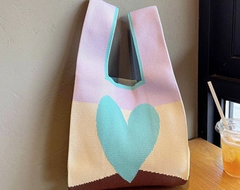 May include: A knitted tote bag with a large heart design in shades of light blue, brown, cream, and purple. The bag has two handles.